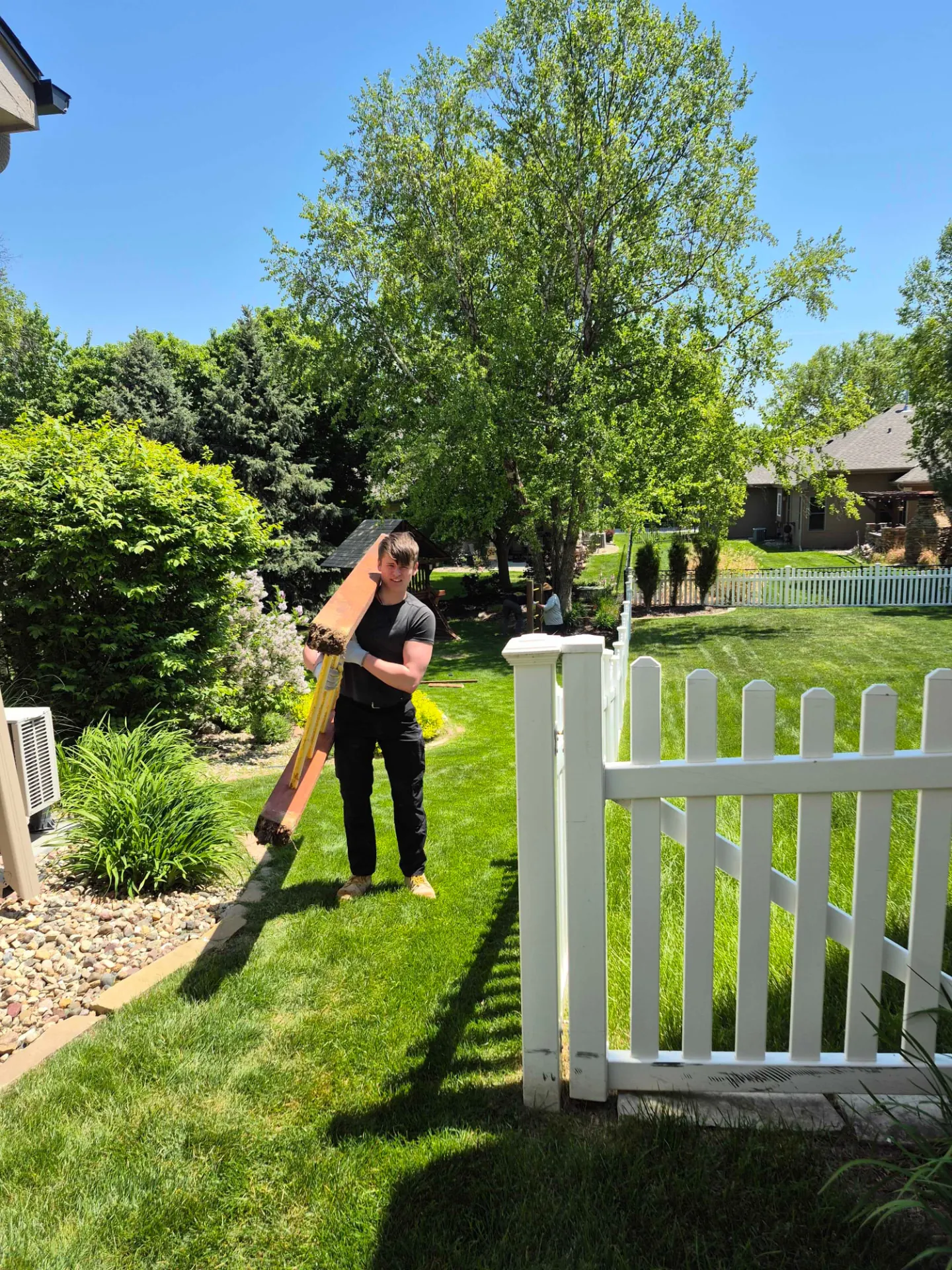 Crew member carrying deck boards out of a backyard on a Ralston project