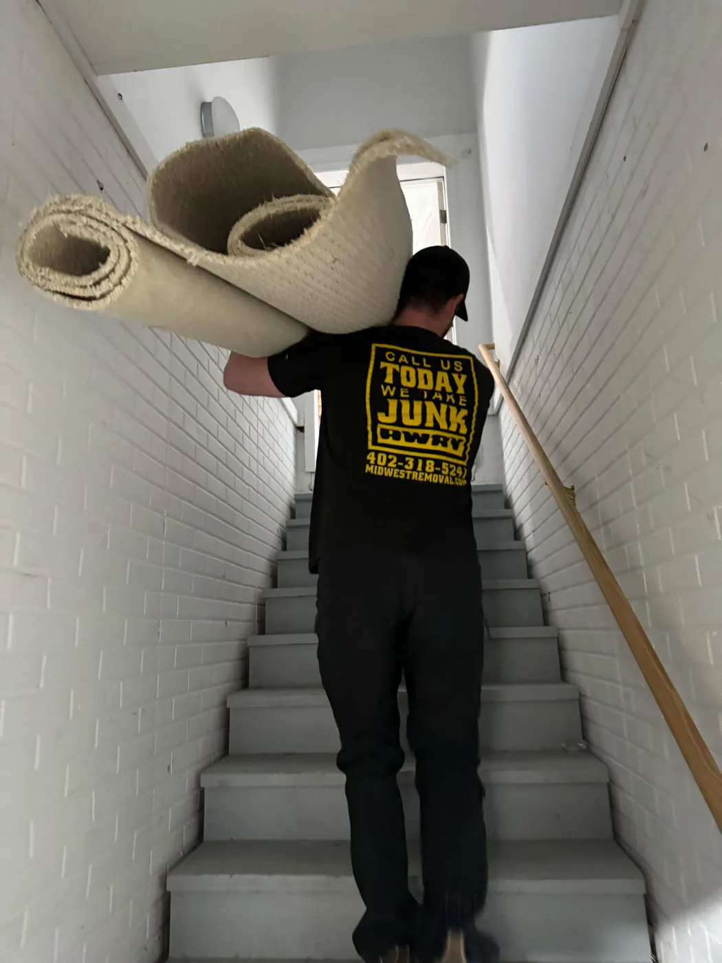 Midwest Removal crew carrying rolled carpet up a stairwell in Omaha