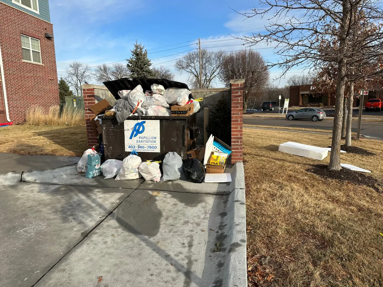 Overflowing dumpster with bagged trash and boxes stacked beside it at an Omaha property