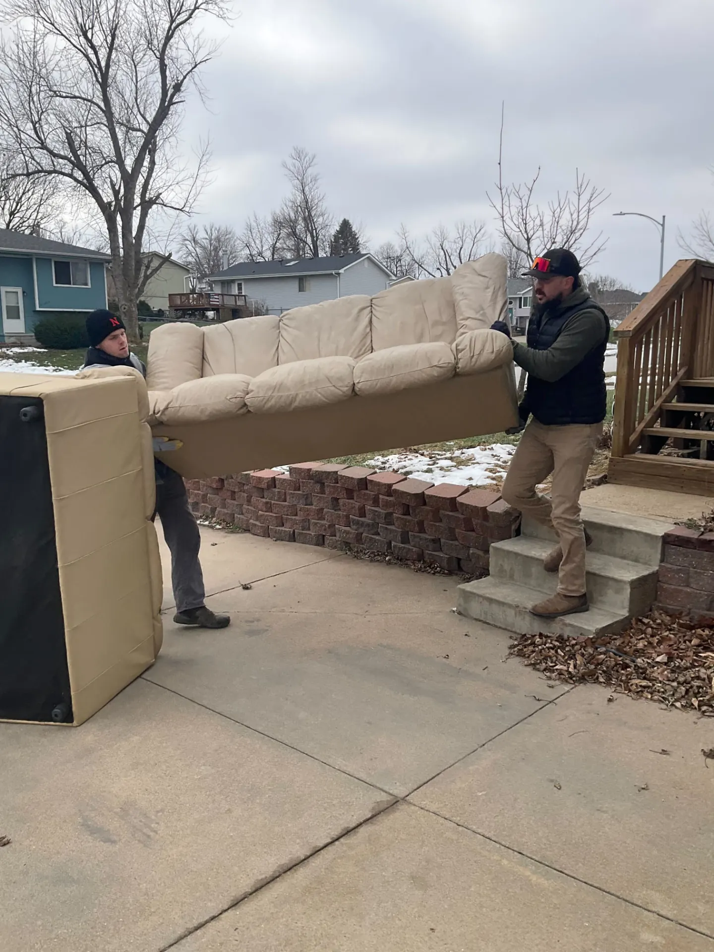 Two crew members carrying a couch and mattress down a driveway