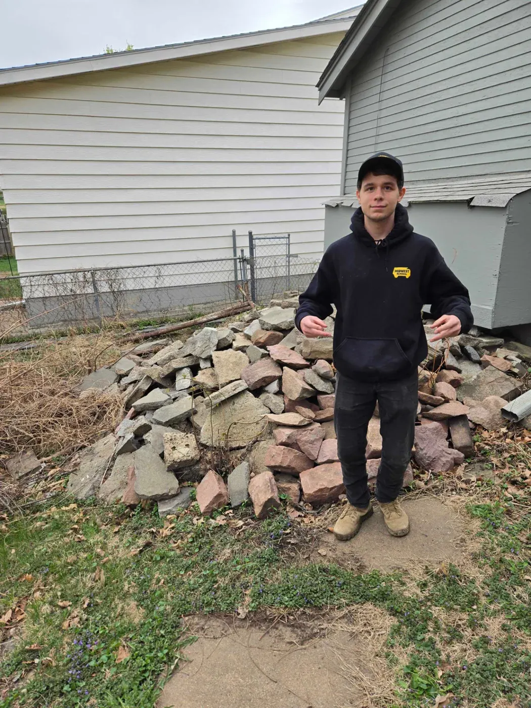 Midwest Removal crew member beside a pile of broken concrete and stone in an Omaha back yard